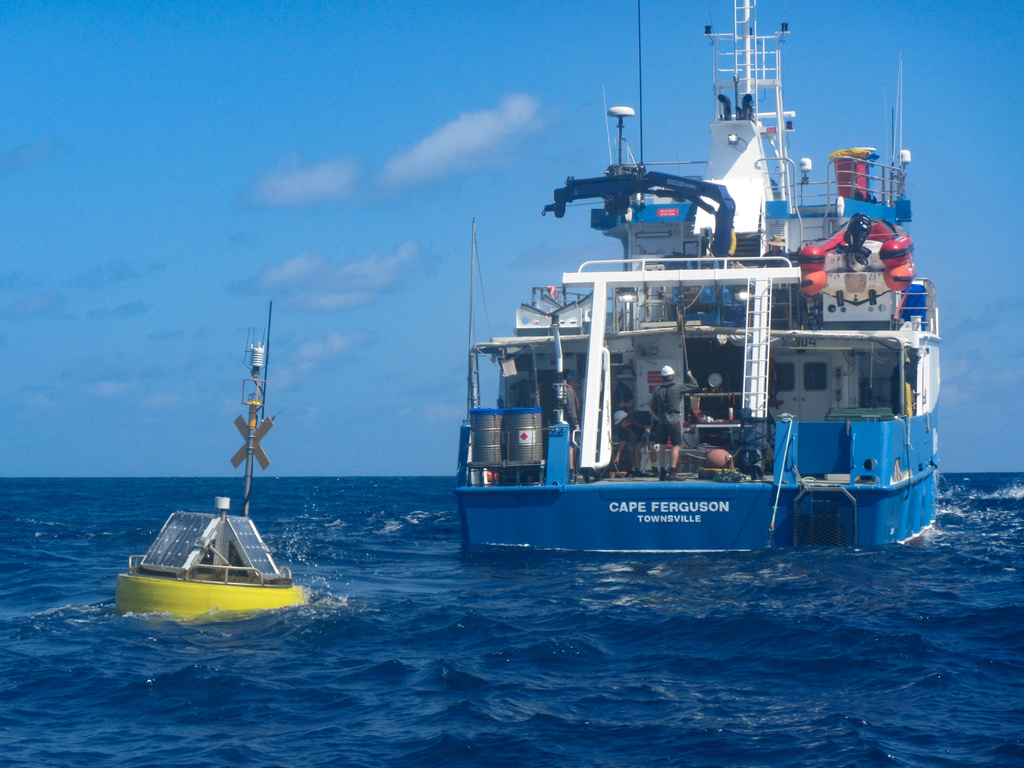 A yellow buoy floating near a blue research vessel.